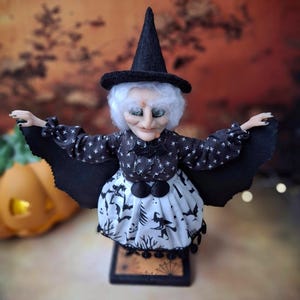 Top-down view of the handmade witch art doll, showing her witch-themed Halloween outfit, hand-painted face, and fully spread bat wings.