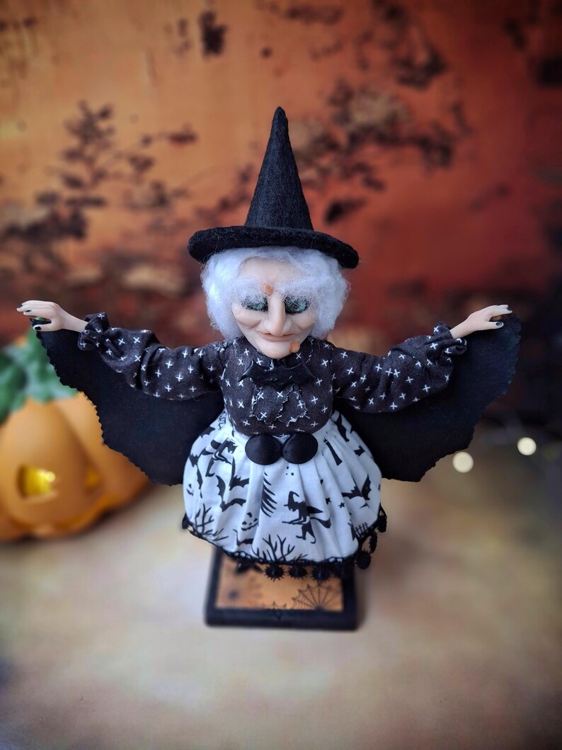 Top-down view of the handmade witch art doll, showing her witch-themed Halloween outfit, hand-painted face, and fully spread bat wings.