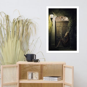 May include: A surreal digital art print featuring a creature with a fox-like head sitting outside a wooden door. The creature is wearing a brown outfit and holding a cigarette. The door is surrounded by vines and a streetlight shines on the scene.