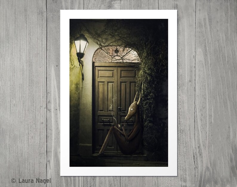 May include: A dark, moody illustration of a creature with a deer-like head sitting outside a wooden door. The creature is wearing a brown, textured outfit and has a cigarette in its mouth. The door is surrounded by overgrown vines and a street lamp casts a warm glow on the scene.