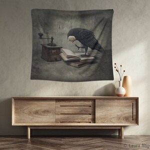 May include: A black and white tapestry featuring a bird with a human-like face looking at an open book and a vintage coffee grinder. The background is a textured gray wall.