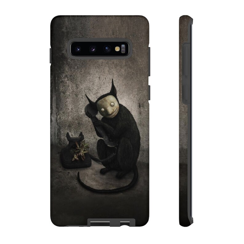 May include: A black phone with a black cat with a white mask holding the receiver to its ear. The cat is sitting on a gray concrete surface.