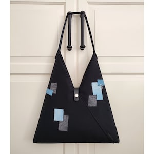 May include: A black triangular tote bag with blue and gray fabric patches. The bag has a black strap and a silver buckle.