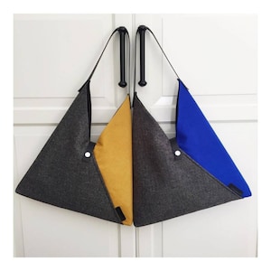 May include: Two triangular-shaped tote bags with black straps. One bag is gray with a yellow panel, and the other is gray with a blue panel.