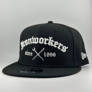 May include: Black fitted baseball cap with a white embroidered logo that says "Ironworkers Since 1896" with a wrench and hammer crossed underneath the text.