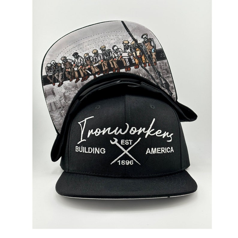 May include: Black and white baseball cap with a white embroidered logo that says "Ironworkers Building America Est. 1896". The back of the cap features a graphic of a group of men sitting on a beam.