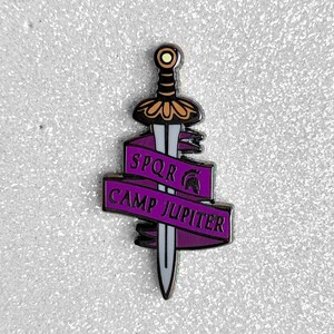 May include: Purple enamel pin featuring a silver sword and a banner that reads "SPQR CAMP JUPITER".