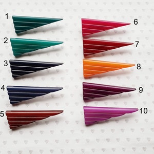 May include: A collection of ten vintage Art Deco style barrettes in various colors. Each barrette is a triangular shape with horizontal lines. Colors include green, blue, red, orange, and purple.