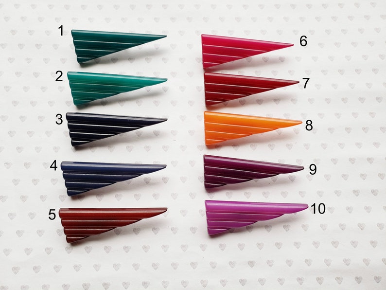 May include: A collection of ten vintage Art Deco style barrettes in various colors. Each barrette is a triangular shape with horizontal lines. Colors include green, blue, red, orange, and purple.
