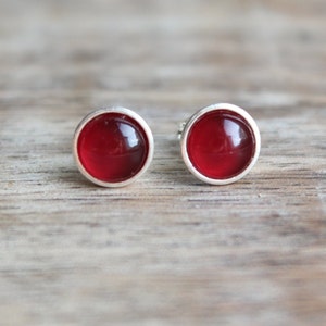 May include: A pair of silver stud earrings with red round glass stones.