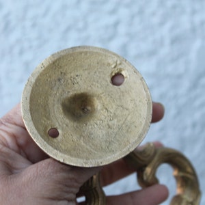 Pu&ograve; includere: Il lato inferiore di una maniglia per porta in ottone con un design decorativo. La maniglia ha due fori per le viti per il montaggio.