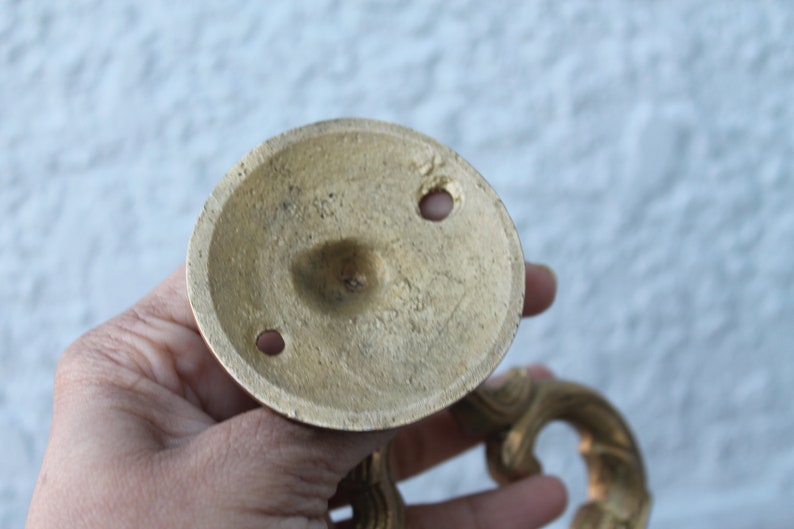Pu&ograve; includere: Il lato inferiore di una maniglia per porta in ottone con un design decorativo. La maniglia ha due fori per le viti per il montaggio.