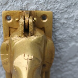 May include: A gold-colored metal door knocker shaped like an elephant's head with a trident symbol on the forehead.