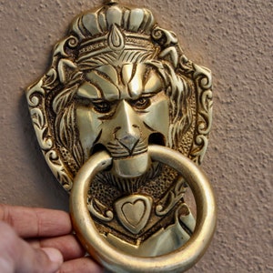 May include: A gold lion's head door knocker with intricate details and a ring pull. The lion is wearing a crown and has a fierce expression.