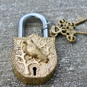 May include: A gold padlock with a bird design on the front. The padlock has a silver shackle and comes with two ornate keys.