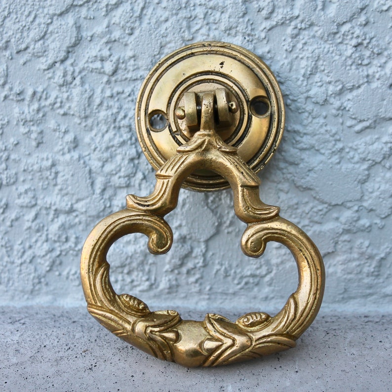 Pu&ograve; includere: Un batacchio per porta dorato con un design decorativo e ornato. Il batacchio ha la forma di un cuore con dettagli intricati e una base rotonda.