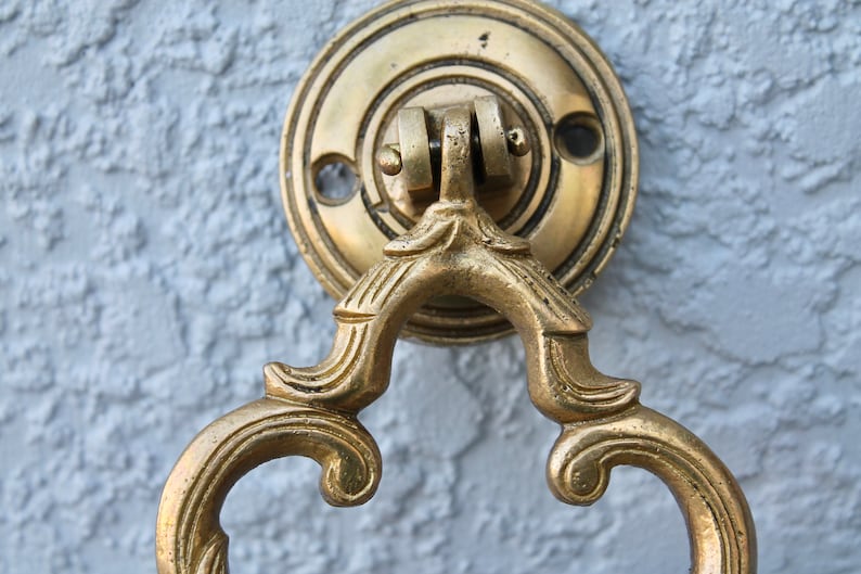 Pu&ograve; includere: Un batacchio per porta dorato con un designo decorativo e ornato. Il batacchio &egrave; attaccato a una piastra rotonda in ottone.