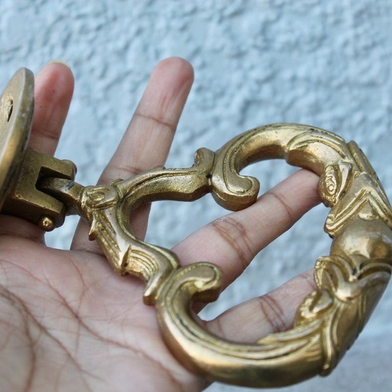 Pu&ograve; includere: Un batacchio per porta in metallo dorato con un design ornamentale. Il batacchio ha la forma di un cuore con un'impugnatura ad anello decorativo.