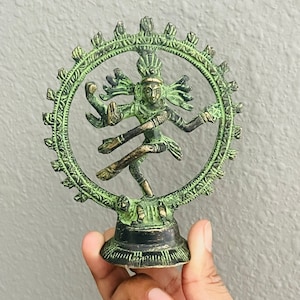 May include: Green metal statue of Shiva Nataraja, the Hindu god of dance, in a circular pose with multiple arms. The statue is on a round base.