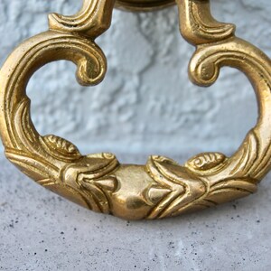 Pu&ograve; includere: Un batacchio per porta dorato ornato con un designo decorativo. Il batacchio ha la forma di un cuore stilizzato con un'impugnatura ad anello.