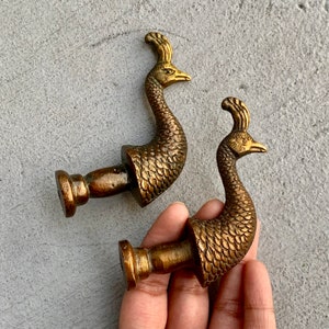May include: Two gold-toned peacock-shaped door knobs. The knobs are detailed with intricate feather patterns and have a smooth, polished finish.