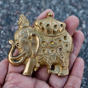 Może przedstawiać: Szczegółowa, złota figurka słonia z misternymi rzeźbami. Słoń ma dekoracyjną koronę i siodło i jest trzymany w dłoni. Figurka jest prawdopodobnie wykonana z metalu i ma wygląd vintage lub antyczny.