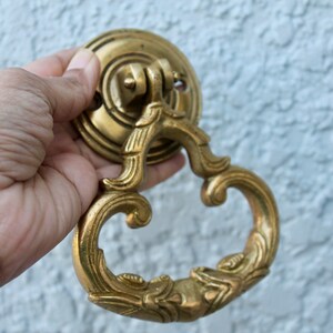 Pu&ograve; includere: Un batacchio per porta decorato in oro con un design a spirale. Il batacchio ha una base rotonda e un'impugnatura a forma di anello.