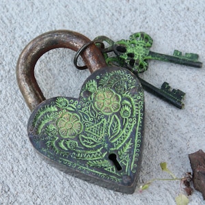 May include: A heart-shaped brass padlock with intricate green floral designs and two matching keys. The padlock has a keyhole and is a vintage style.