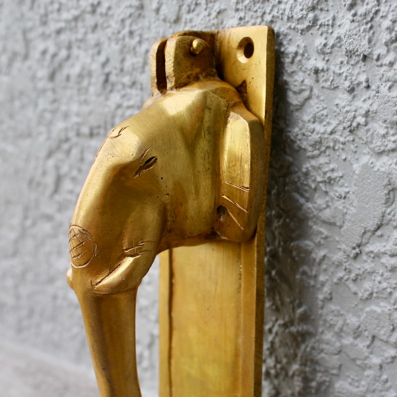 May include: A gold-toned door handle shaped like an elephant's head. The handle is mounted on a rectangular plate.