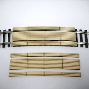 May include: A set of five wooden track pieces for model train layouts. The pieces are designed to create a curved track section. The pieces are made of light brown wood and have a natural finish.