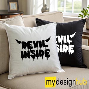 Könnte beinhalten: Zwei Kissen auf einem beigen Sofa. Ein Kissen ist weiß mit dem Text "DEVIL INSIDE" in Schwarz, und das andere ist schwarz mit dem Text "EVIL SIDE" in Weiß. Beide Texte haben einen Tropfeffekt.