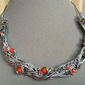 May include: A silver wire necklace with orange beads. The necklace is made of twisted wire and has a delicate, flowing design.