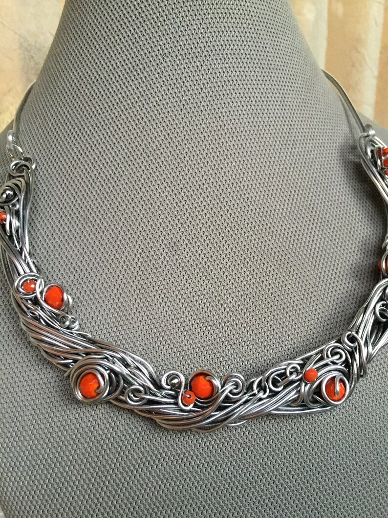 May include: A silver wire necklace with orange beads. The necklace is made of twisted wire and has a delicate, flowing design.