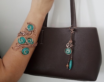 May include: Copper arm cuff and purse charm with turquoise accents. The arm cuff features an open design with swirling patterns and turquoise stone inlays. The purse charm has a matching design, hanging from a brown leather handbag.