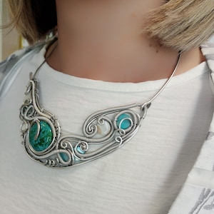 May include: A handcrafted silver wire necklace with a large, round, turquoise-coloured stone and smaller turquoise and white stones. The necklace has a unique, swirling design.