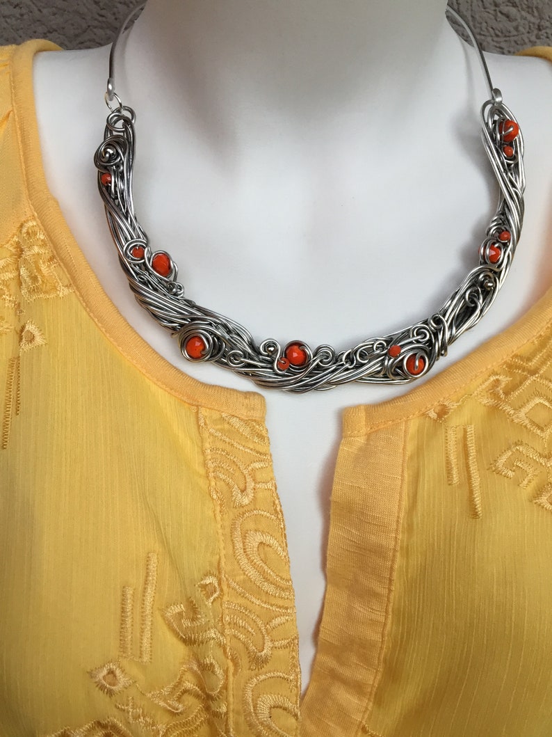May include: A silver wire necklace with orange beads. The necklace is in the shape of a crescent moon and is on a white mannequin.