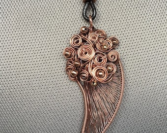 May include: A copper wire pendant necklace with a cluster of copper wire spirals and beads. The pendant is shaped like a teardrop and hangs from a black leather cord.