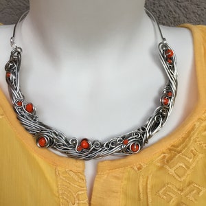 May include: A silver wire necklace with orange beads. The necklace is in the shape of a crescent moon and is made of wire that has been twisted and woven together.