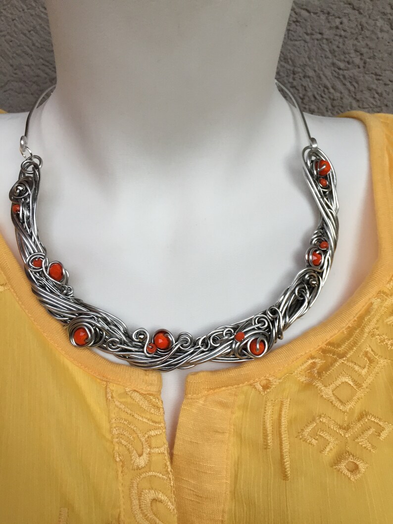 May include: A silver wire necklace with orange beads. The necklace is in the shape of a crescent moon and is made of wire that has been twisted and woven together.