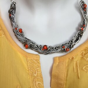 May include: A silver wire necklace with orange beads. The necklace is in the shape of a crescent moon and has a delicate, intricate design.