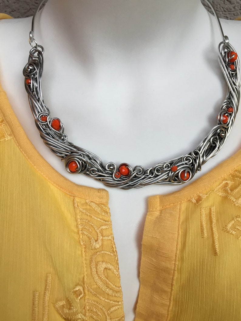 May include: A silver wire necklace with orange beads. The necklace is in the shape of a crescent moon and has a delicate, intricate design.