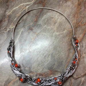 May include: A silver wire necklace with orange beads. The necklace is made of wire that is twisted and woven together to create a unique design. The beads are small and round, and they are evenly spaced along the necklace.