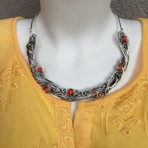 May include: A silver wire necklace with orange beads. The necklace is in the shape of a crescent moon and is made of twisted wire.