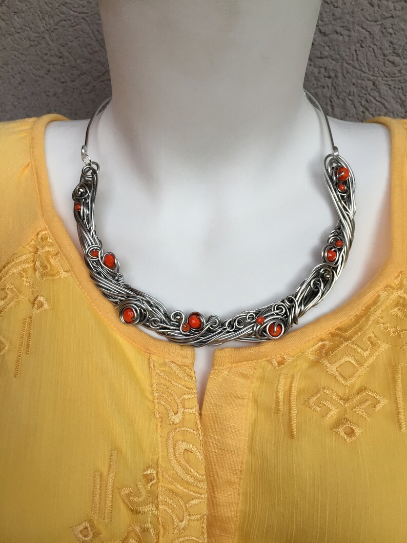 May include: A silver wire necklace with orange beads. The necklace is in the shape of a crescent moon and is made of twisted wire.