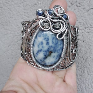 May include: A silver wire wrapped bracelet with a large oval blue and white gemstone. The bracelet is decorated with smaller blue beads and silver wire accents.