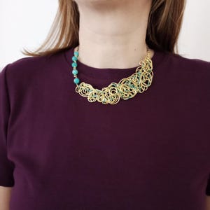 May include: A gold-coloured statement necklace featuring turquoise beads and a swirling wire design. The necklace has a series of turquoise beads on one side and a large, intricate wire design with teal accents on the other.