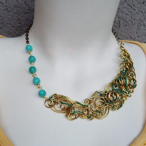 May include: A statement necklace with a gold-toned wire design and turquoise beads. The necklace showcases a distinctive, handcrafted style with a chain fastening. The gold wire is interwoven with green wire, creating a striking contrast.