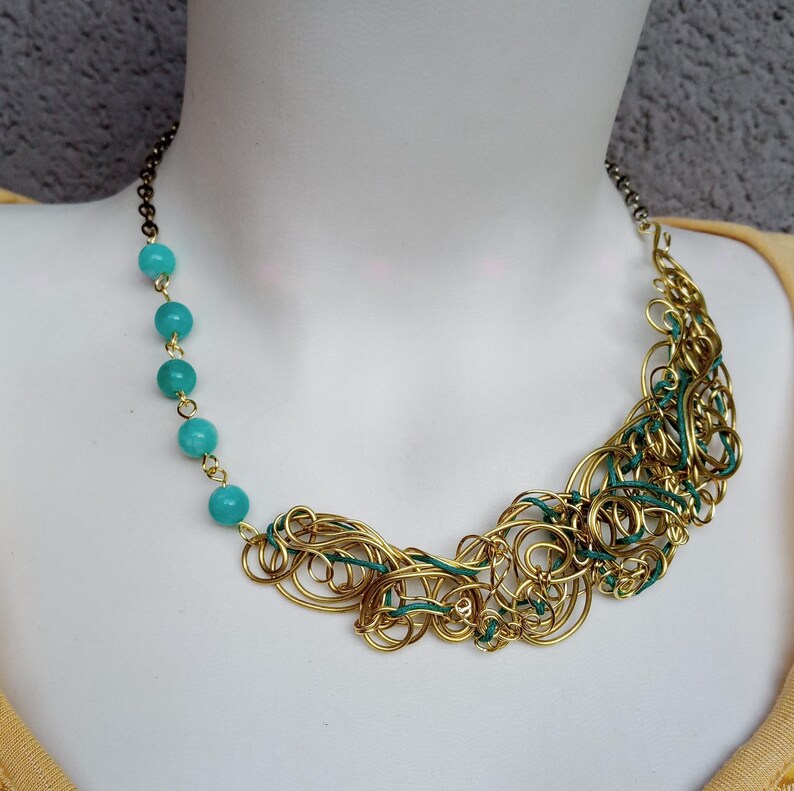 May include: A statement necklace with a gold-toned wire design and turquoise beads. The necklace showcases a distinctive, handcrafted style with a chain fastening. The gold wire is interwoven with green wire, creating a striking contrast.