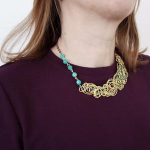 May include: A gold-coloured wire necklace featuring turquoise beads and green detailing. The necklace has an abstract design with loops and curves. Turquoise beads are strung along a chain on one side, creating a striking contrast.