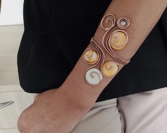 May include: A copper wire bracelet with a swirling design and yellow and white shell accents.
